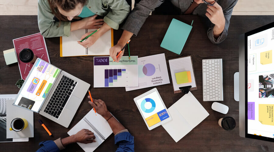 Group of people working around a desk with coffee, laptops and graphs